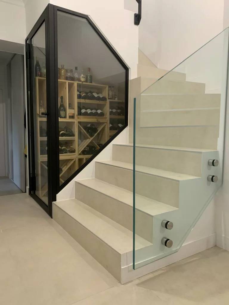 Cave à vin vitrée aménagée sous l'escalier d'une villa contemporaine, casiers à bouteilles derrière le vitrage