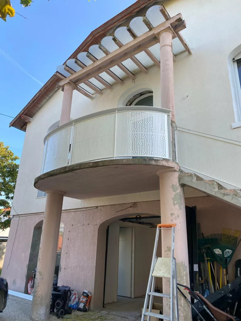 Balcon cintré et son garde-corps en tôle découpée blanche sur la façade de la maison