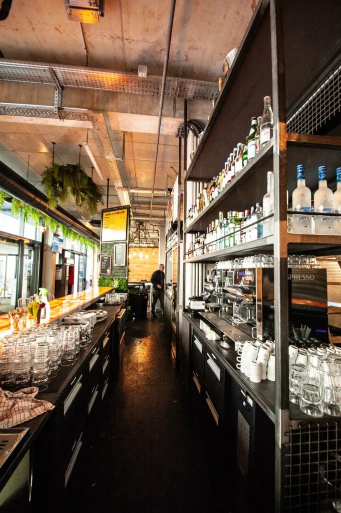 Bar de 40 m² du food court Le Beau Marché à Bourg-en-Bresse : comptoir en enfilade, étagères à bouteilles et verrerie suspendue, fabriqués par BE PROCESS